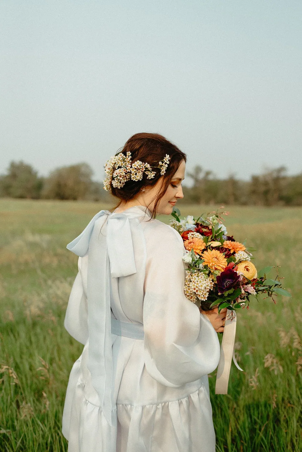 A bride holding a loose bouquet of anemones and blush roses in soft window light