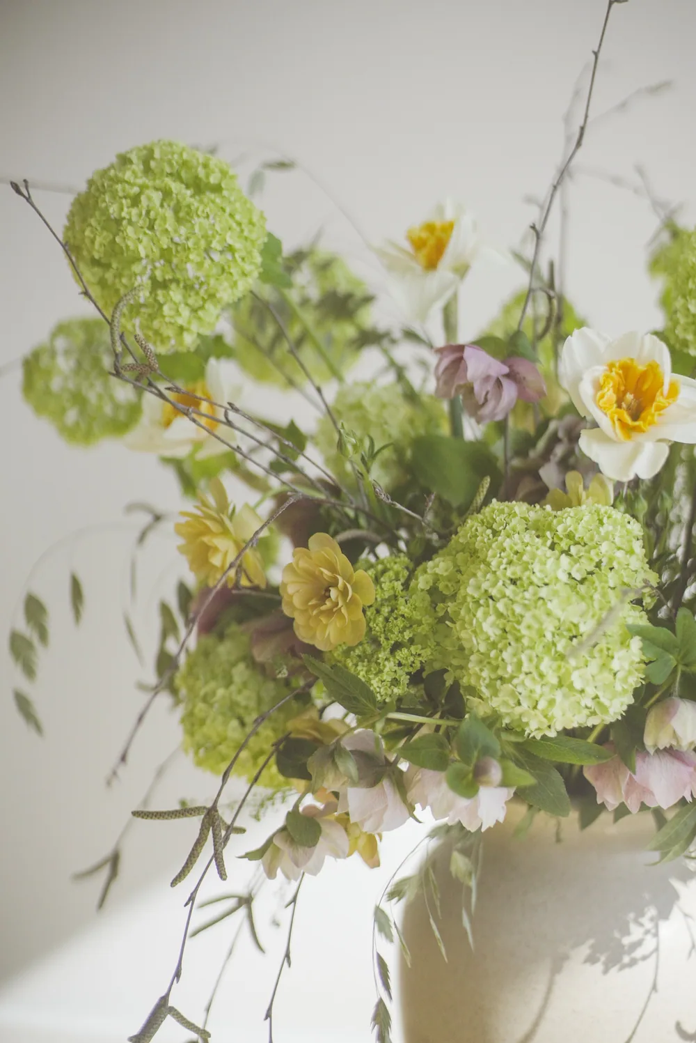 Hands holding a loose green and white arrangement in a pale ceramic vessel